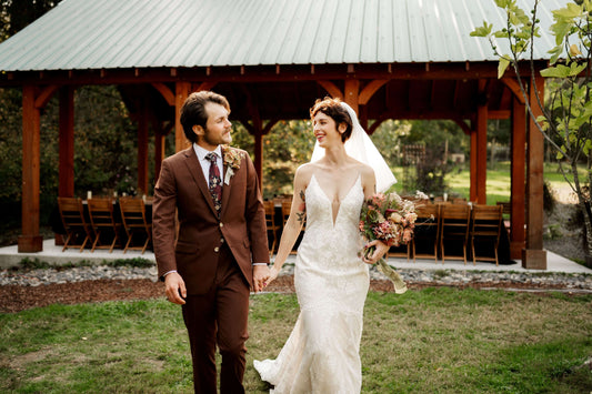 Bride and groom walking in front of open-air reception space with fall-inspired bouquet — Kvetka Flower, rustic Oregon wedding