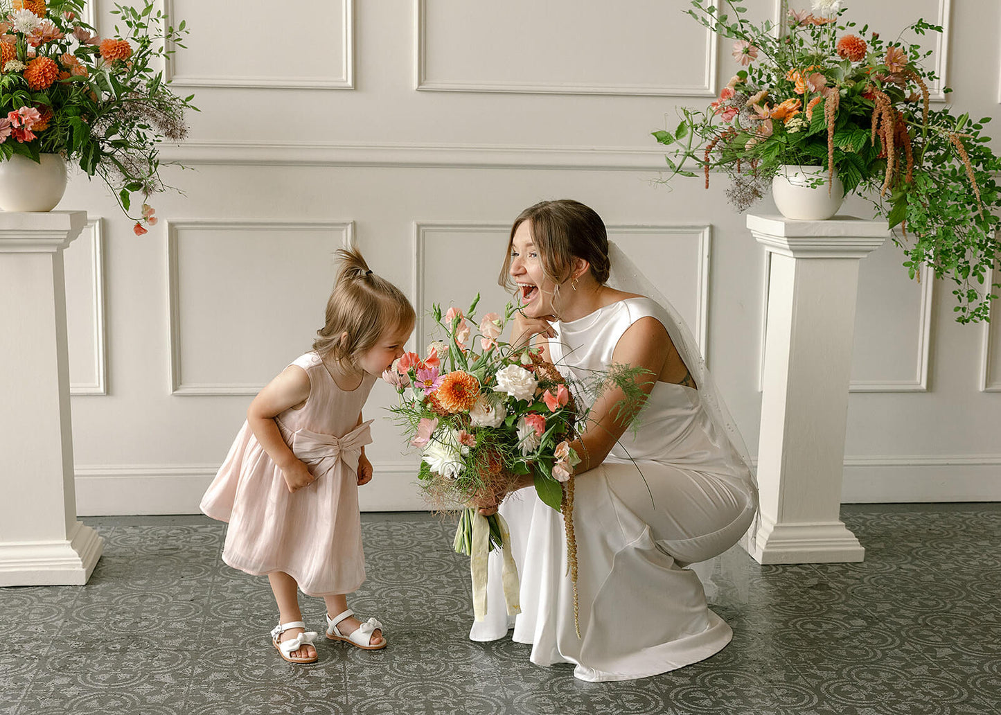 Bride and flower girl in front of floral columns at Tendue, smiling with bouquet