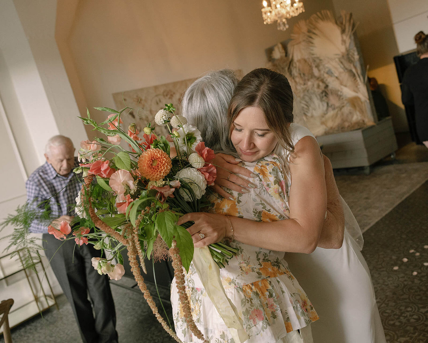Bride hugging guest while holding bridal bouquet with dahlias and sweet peas by Kvetka Flower