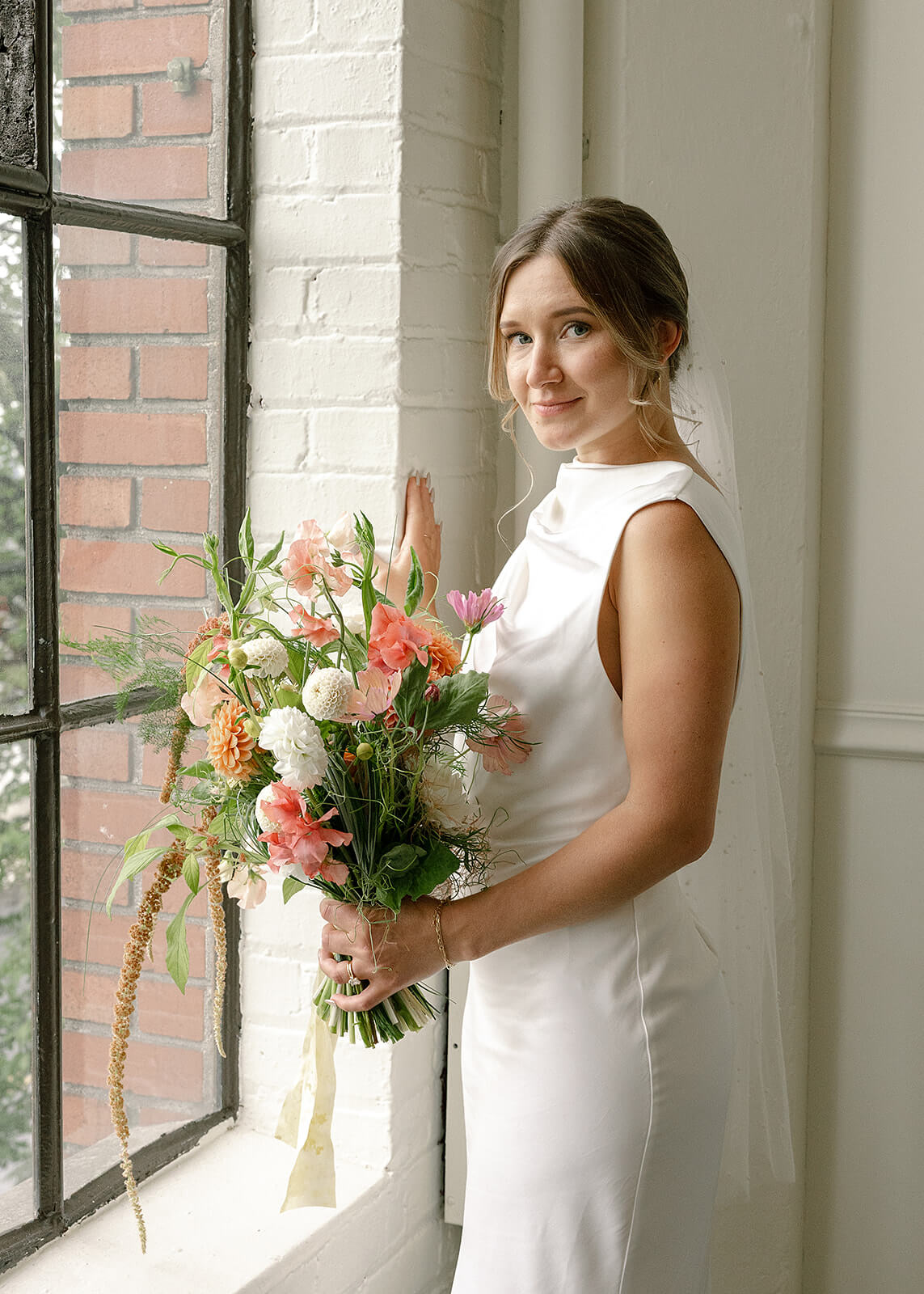 Bride standing near window with soft bridal bouquet at Tendue Portland