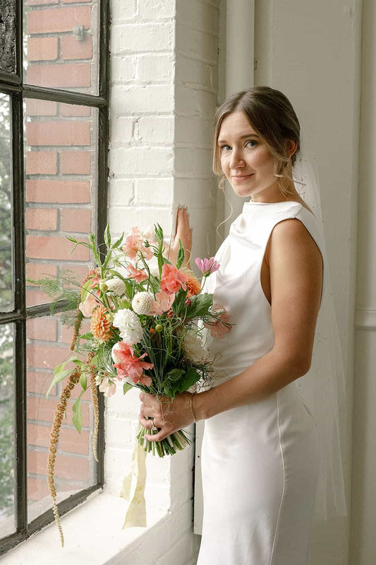 Bride standing near window with soft bridal bouquet at Tendue Portland