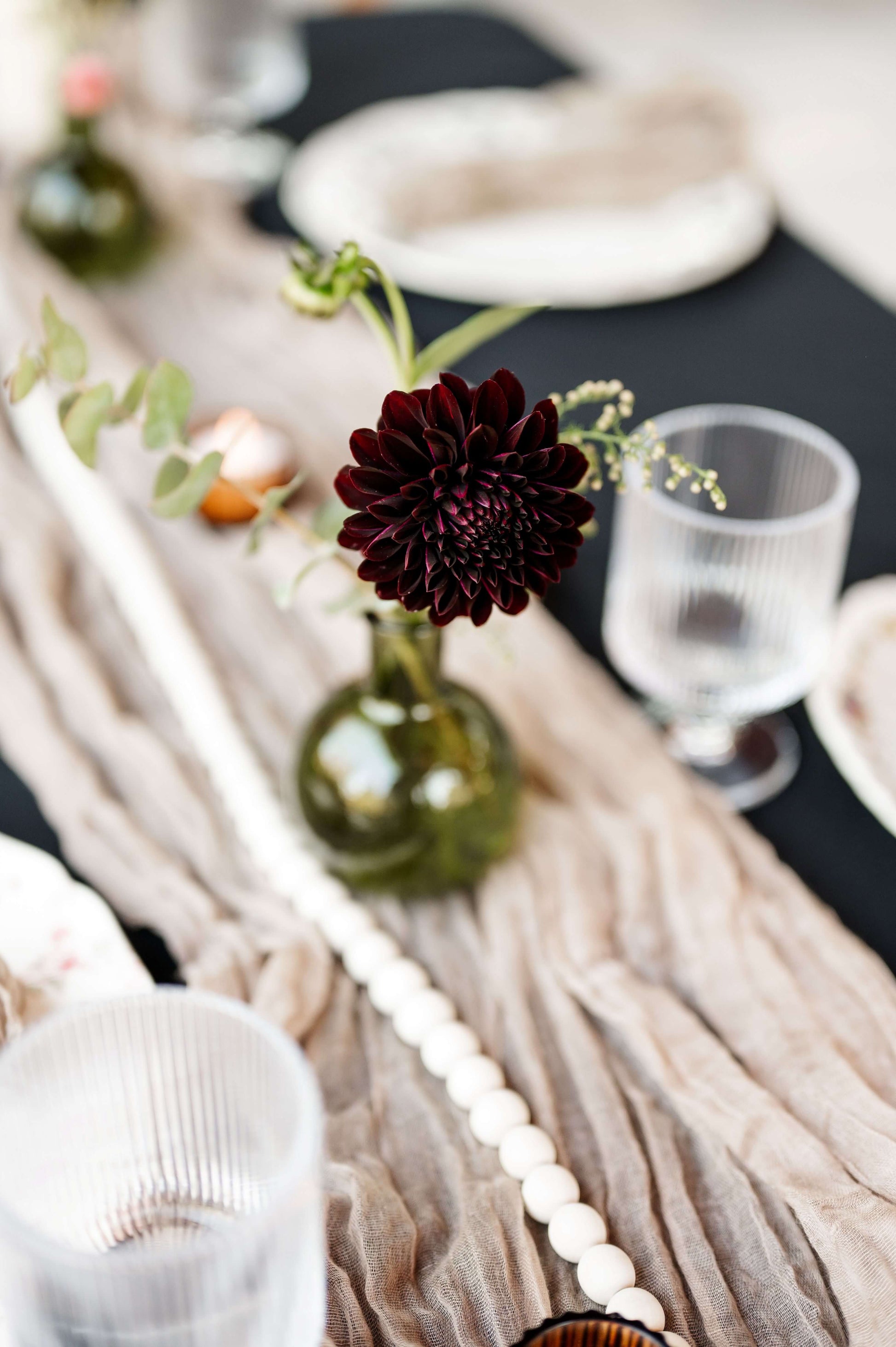 Close-up of burgundy dahlia in green bud vase with soft table runner — Kvetka Flower moody floral decor for fall wedding