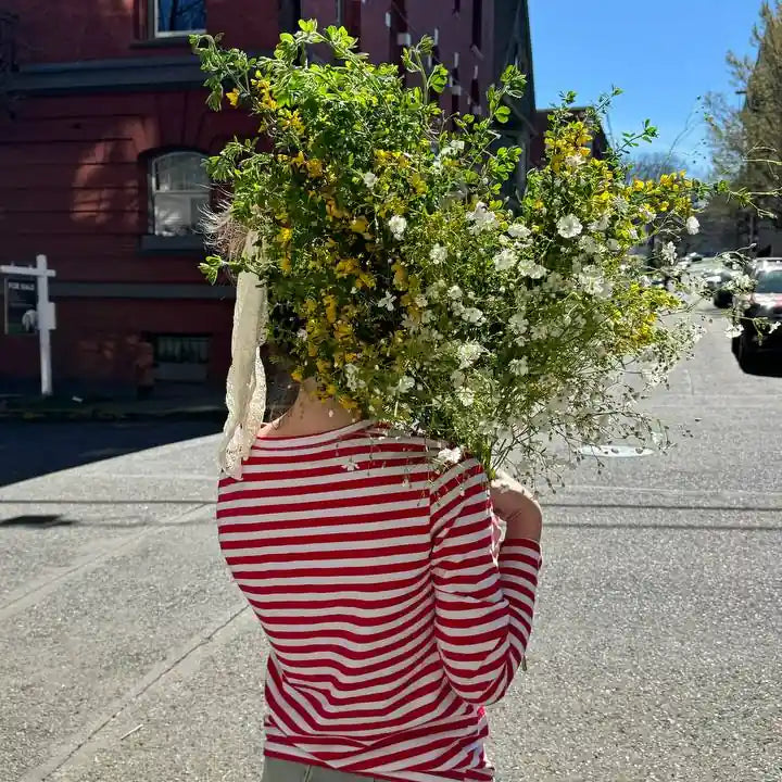 Woman in striped shirt carrying a wildflower bouquet on a sunny street — joyful flower delivery by Kvetka Flower, Portland OR.