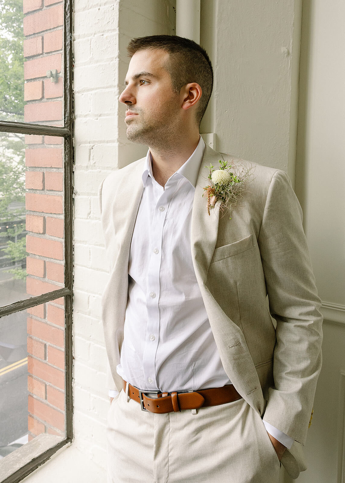 Groom standing near window at Tendue with white dahlia boutonniere by Kvetka Flower