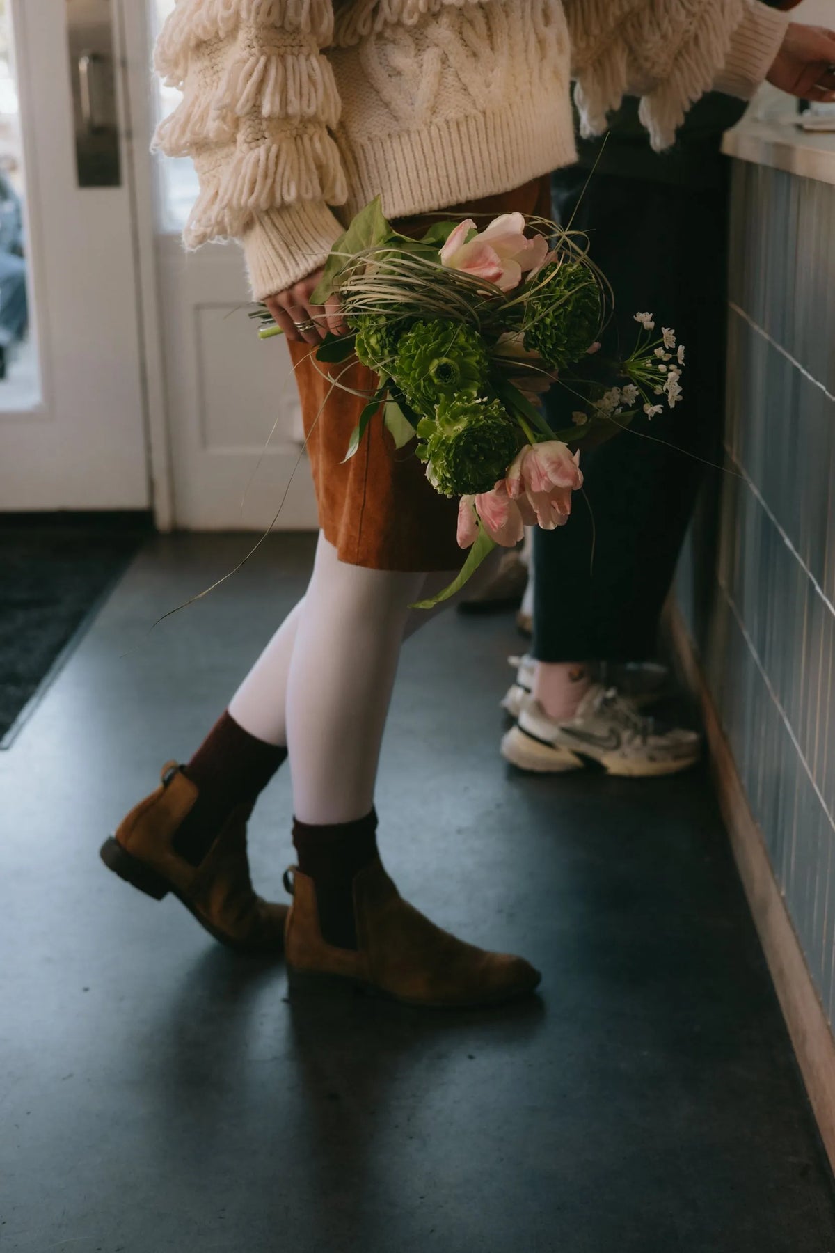 Woman holding green textured bouquet with seasonal blooms in a cafe