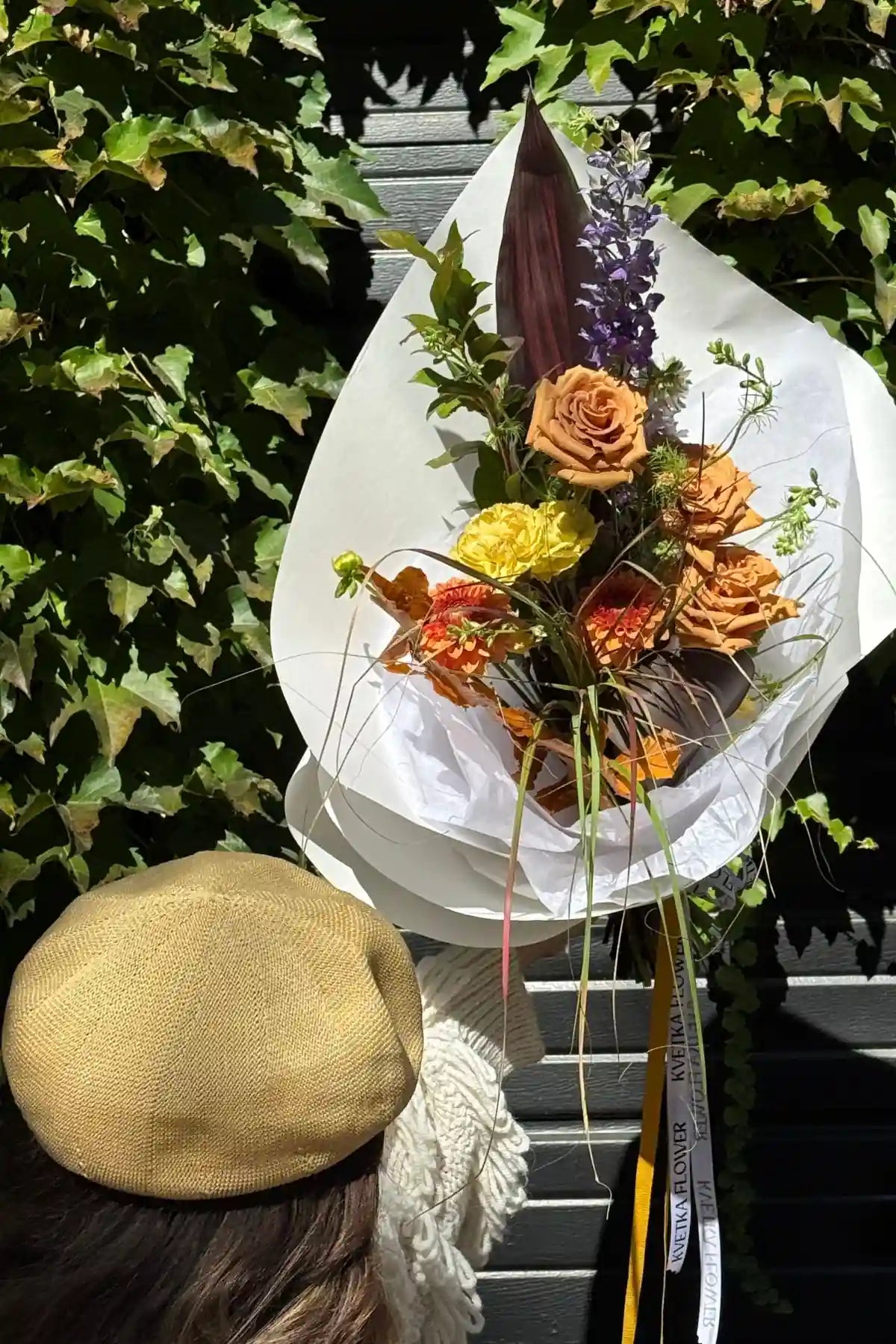 Top view of fresh seasonal bouquet small featuring orange roses, yellow carnations, purple delphinium and autumn greenery