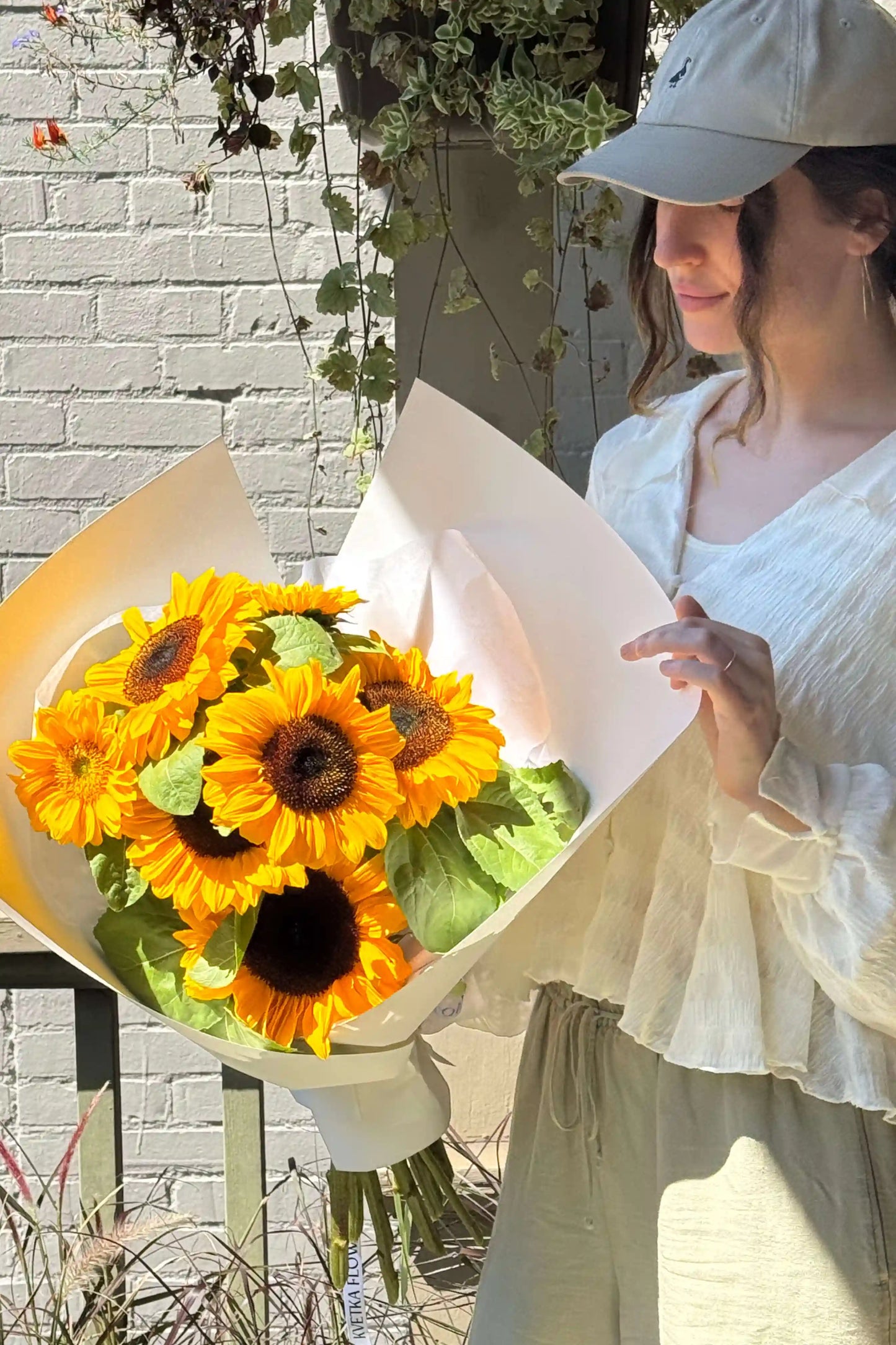 Small sunflower bouquet “Sun Day” from Kvetka Flower, wrapped in white paper, laying on a wooden table – local Portland OR flowers