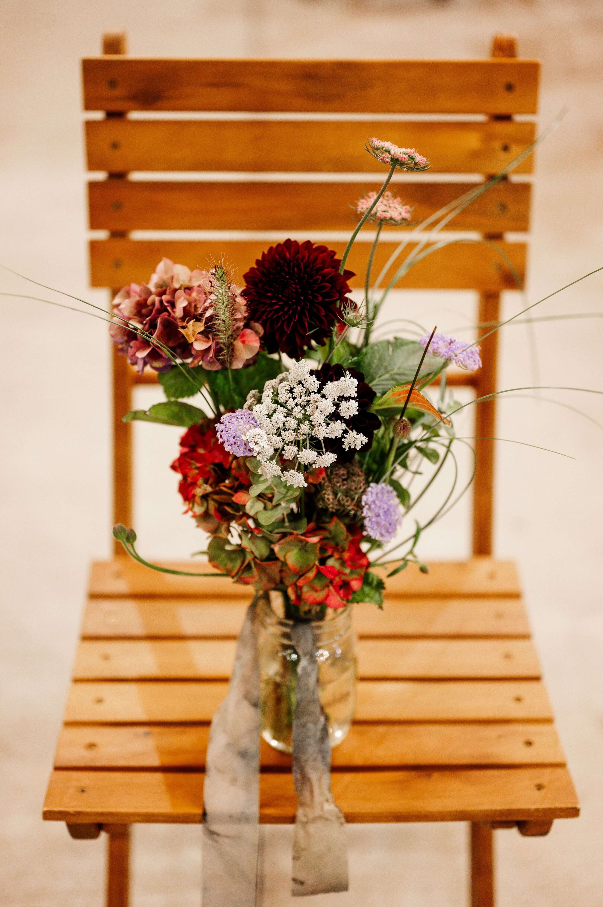 Rustic fall wedding bouquet with dahlias, hydrangeas, and queen anne’s lace in a glass jar on wooden chair — Kvetka Flower, Oregon
