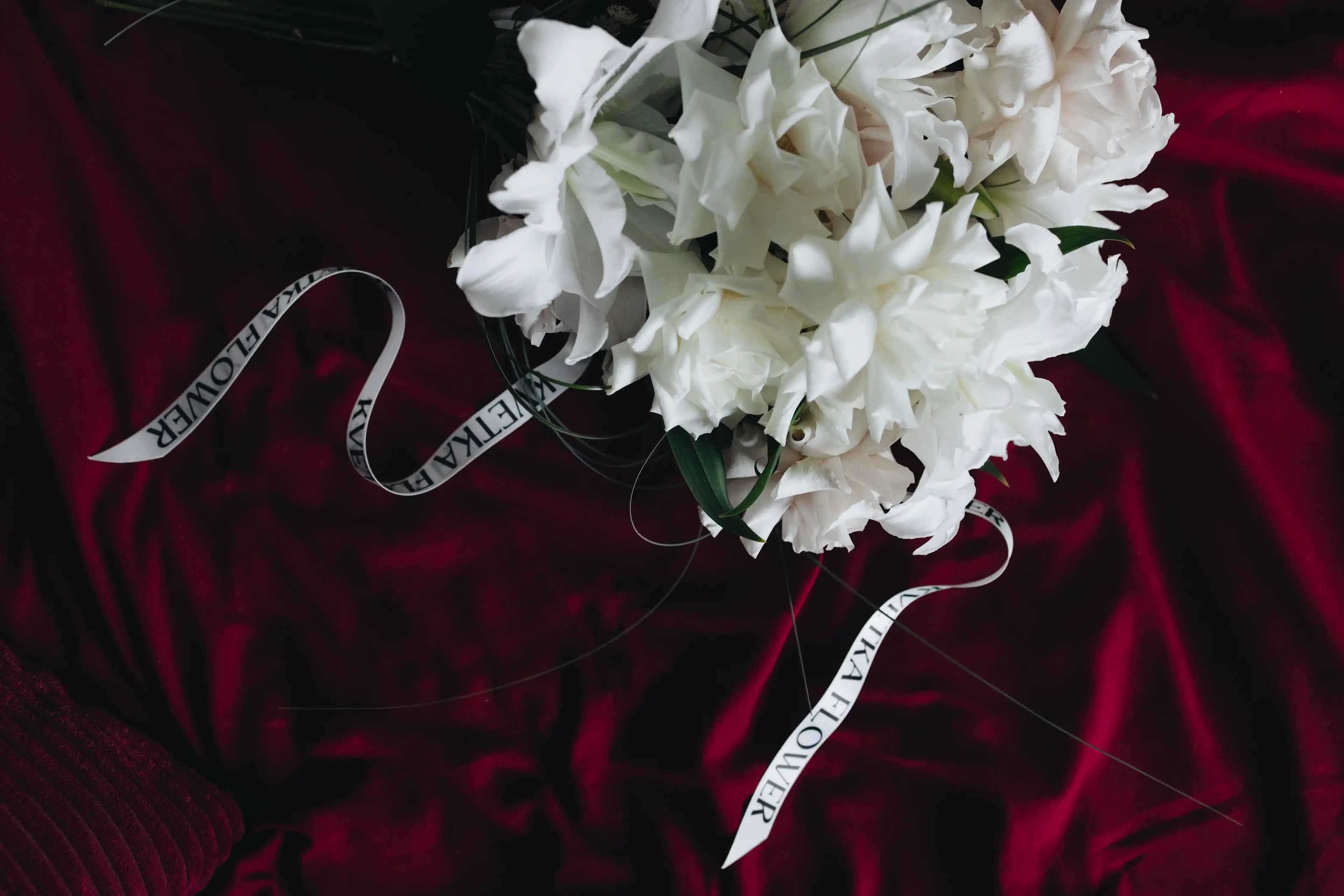 White bouquet made of local lilies with Kvetka Flower ribbon on a deep red background — luxury wedding flowers in Portland, OR.