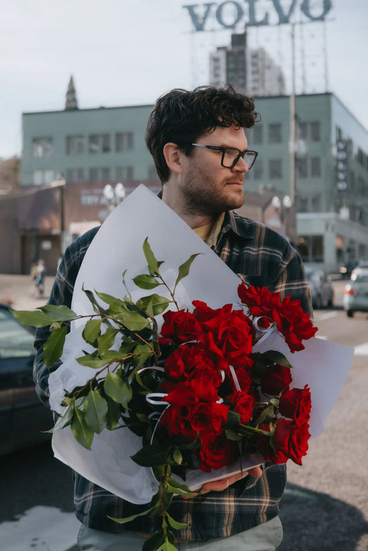 Man holding two dozen red roses with greenery in downtown Portland for Valentine's Day