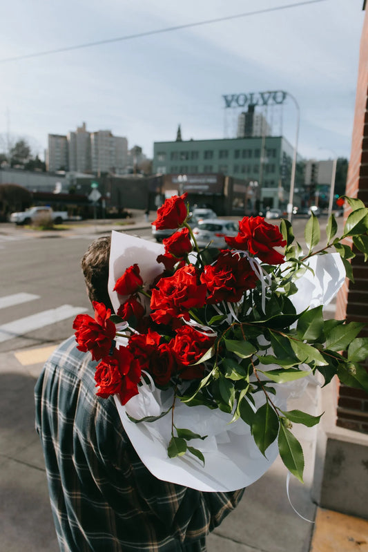 Two dozen red roses with greenery against Portland cityscape