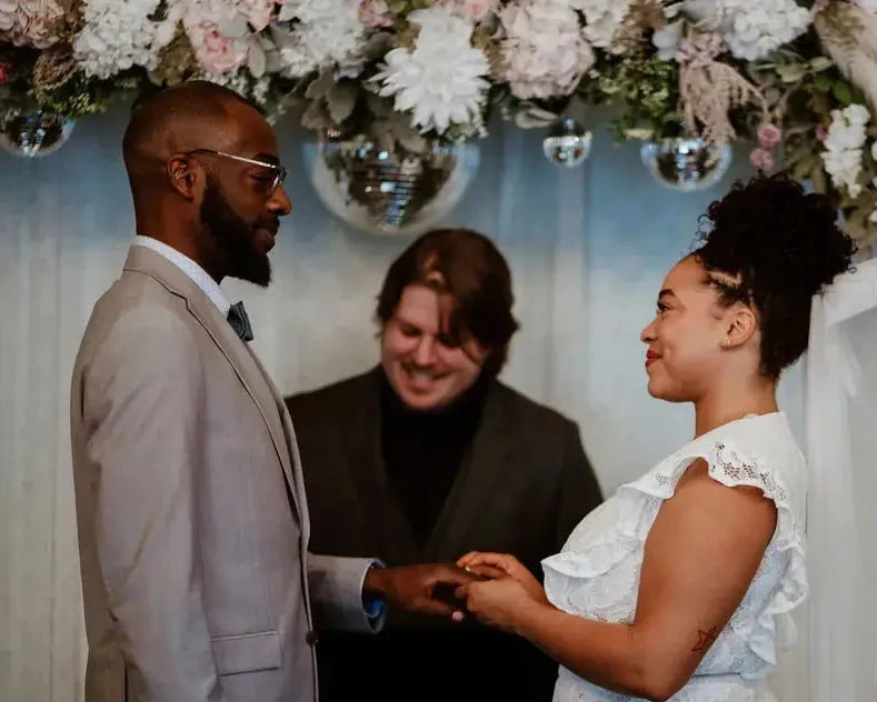 Wedding ceremony with a couple exchanging rings, surrounded by floral decorations.