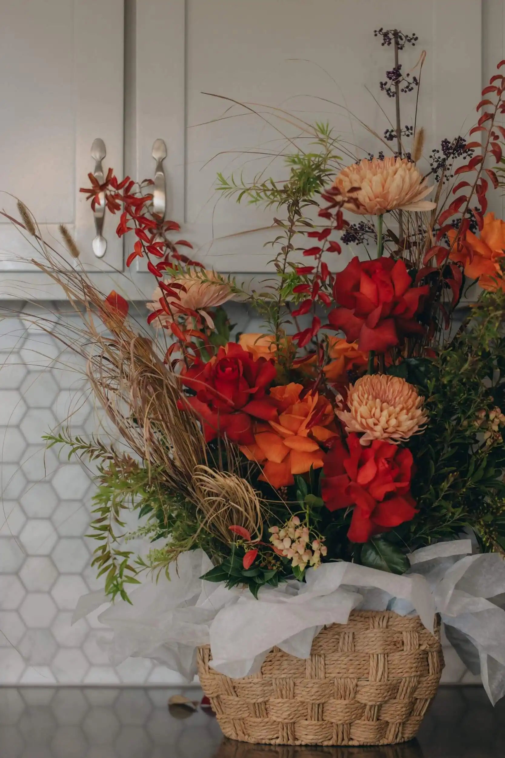 Autumn flower basket with red roses, orange flowers, and seasonal foliage in woven basket