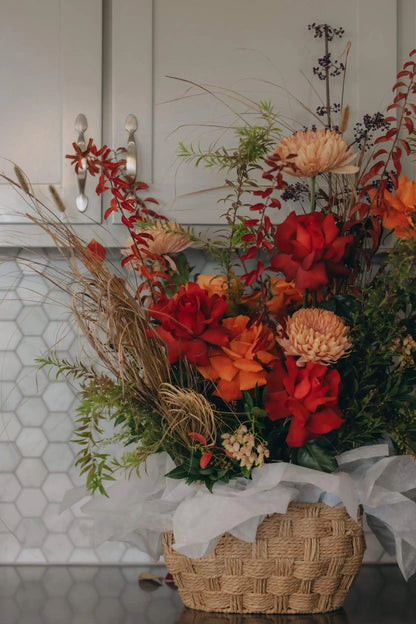 Autumn flower basket with red roses, orange flowers, and seasonal foliage in woven basket