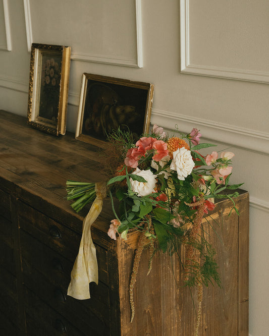 Loose garden-style bridal bouquet placed on wood cabinet near vintage frames
