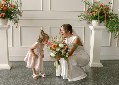 Bride and flower girl in front of floral columns at Tendue, smiling with bouquet