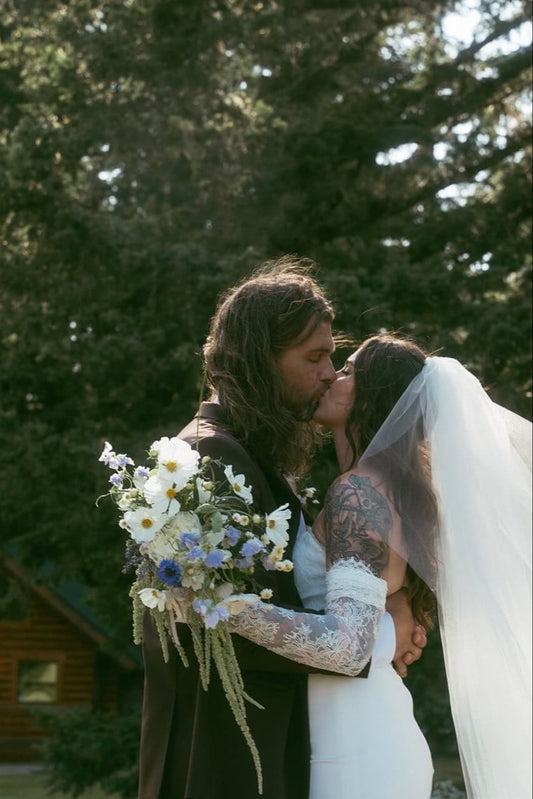 Romantic bride and groom kiss holding bouquet at rustic cabin wedding by Kvetka Flower Portland OR