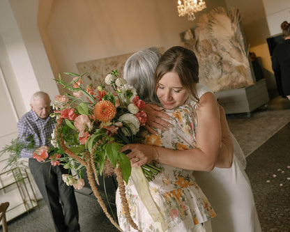 Bride hugging guest while holding bridal bouquet with dahlias and sweet peas by Kvetka Flower