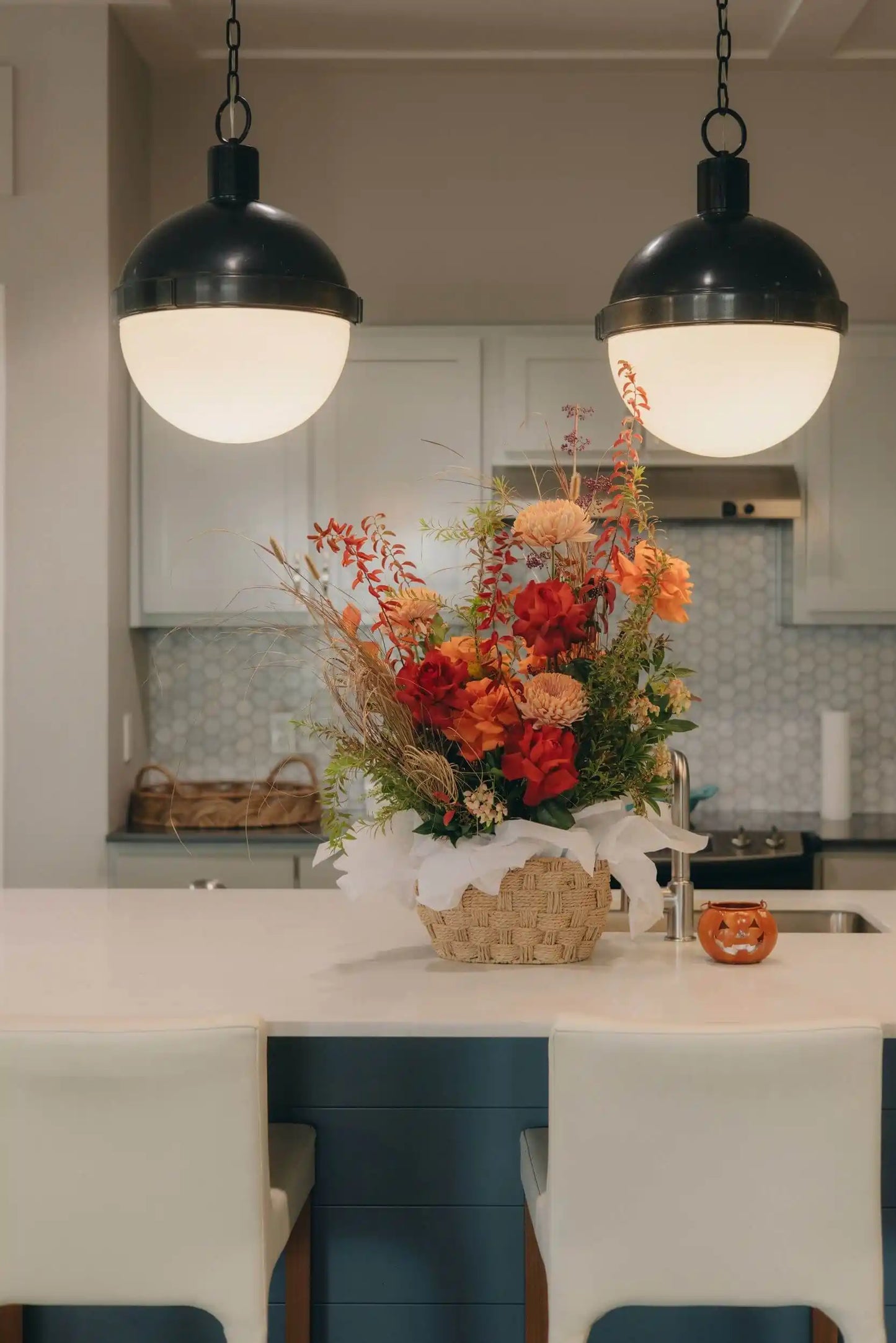 Fall flower basket arrangement with red and orange seasonal flowers on kitchen island centerpiece