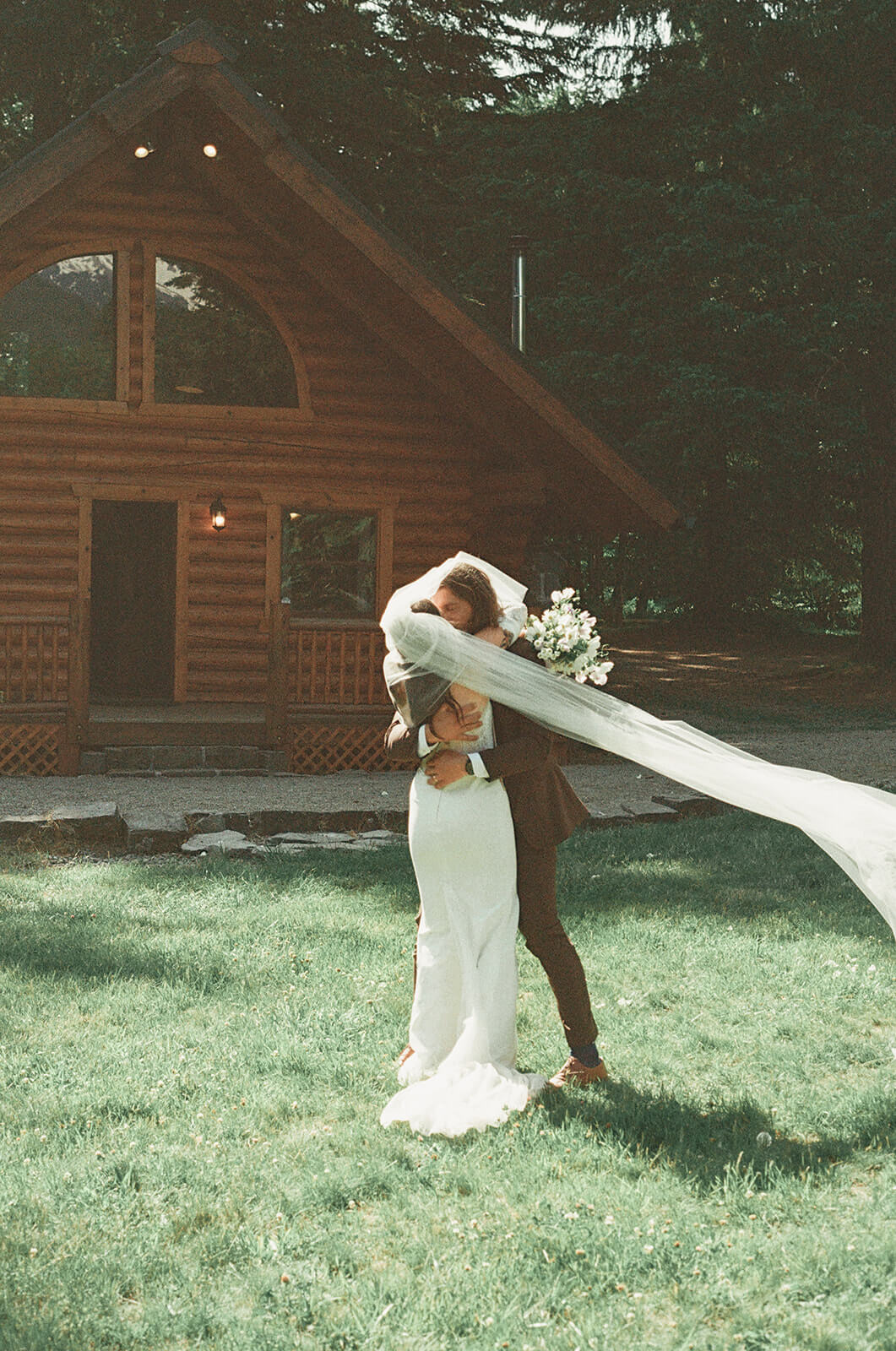 Emotional wedding hug in front of cabin with bridal bouquet designed by Kvetka Flower Portland OR