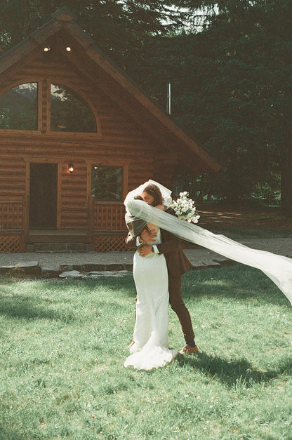Emotional wedding hug in front of cabin with bridal bouquet designed by Kvetka Flower Portland OR