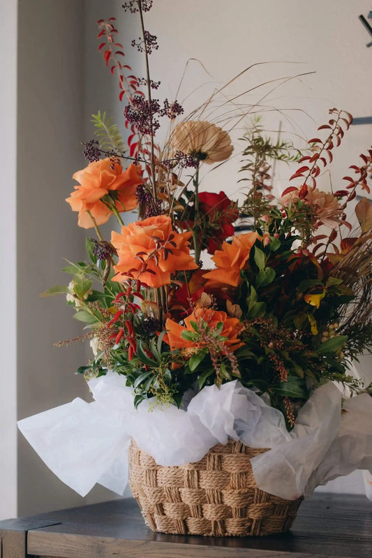 Designer flower basket with red roses, orange blooms, and dried grasses on modern table