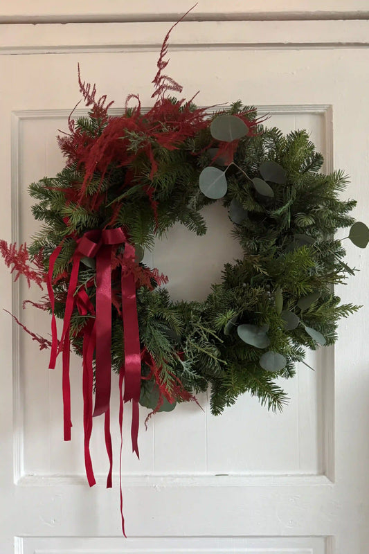 Fresh evergreen Christmas wreath with eucalyptus red accents and burgundy ribbon on white door by Kvetka Flower Portland