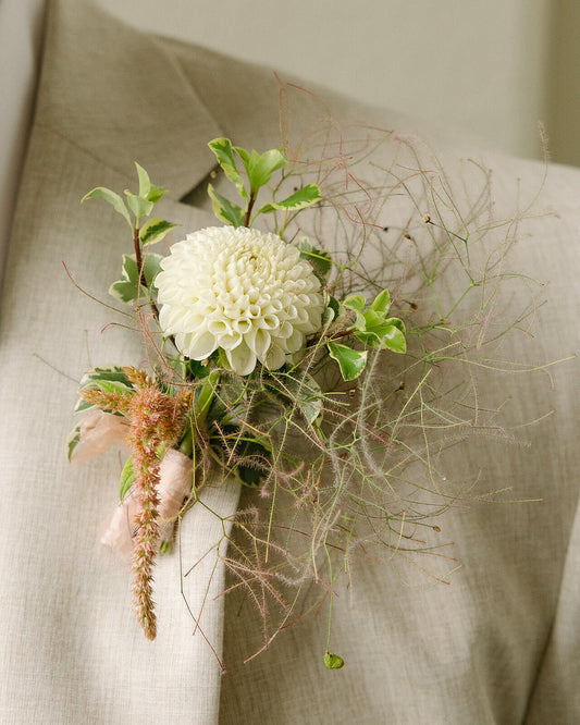 Close-up of groom’s boutonniere with white dahlia, cotinus, and oregonia by Kvetka Flower