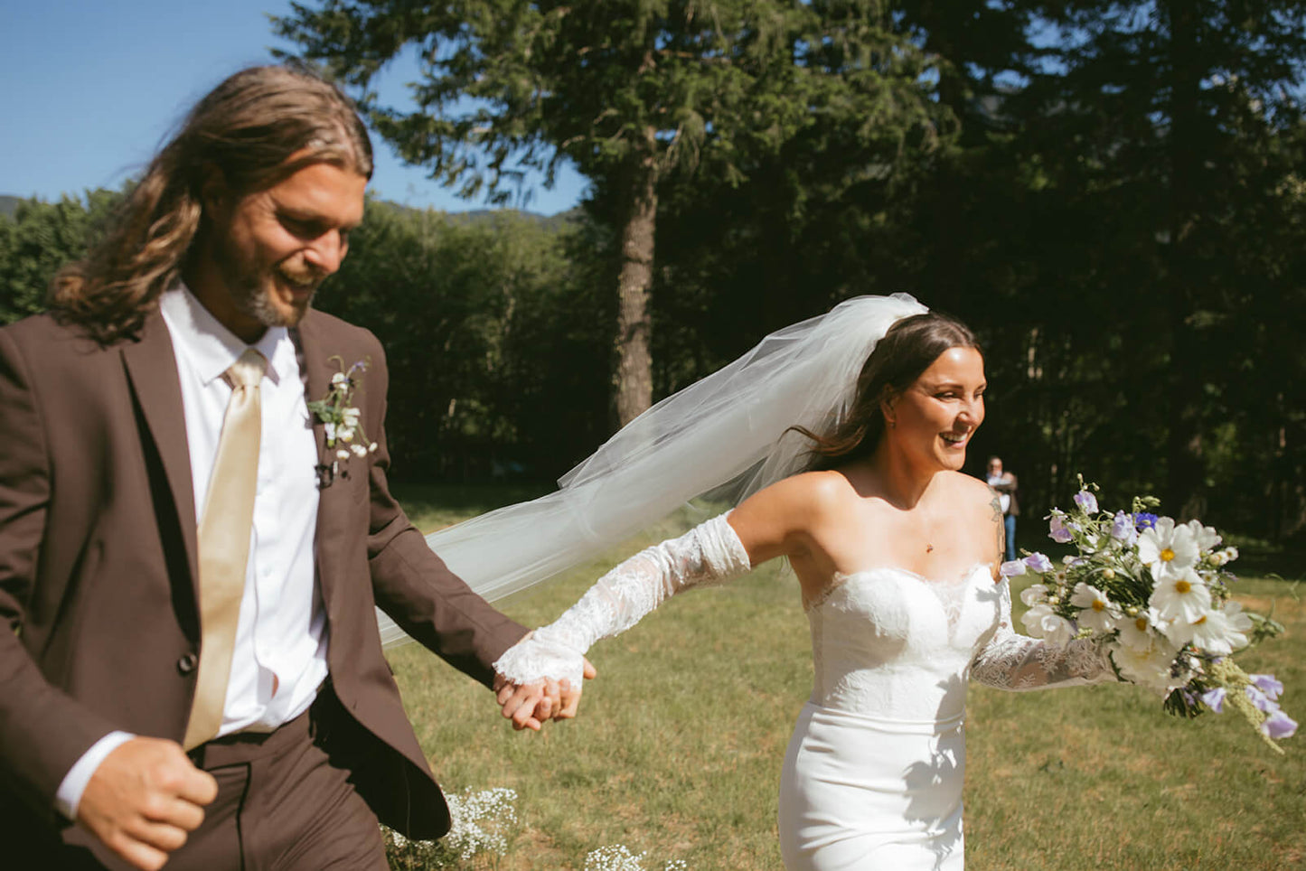 Smiling bride and groom holding bouquet and walking together outdoors with flowers by Kvetka Flower Portland OR