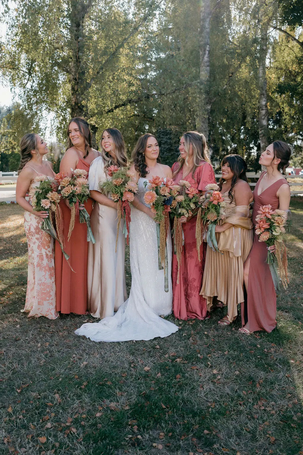 Bride and bridesmaids in mismatched rust and champagne dresses with fall bouquets.