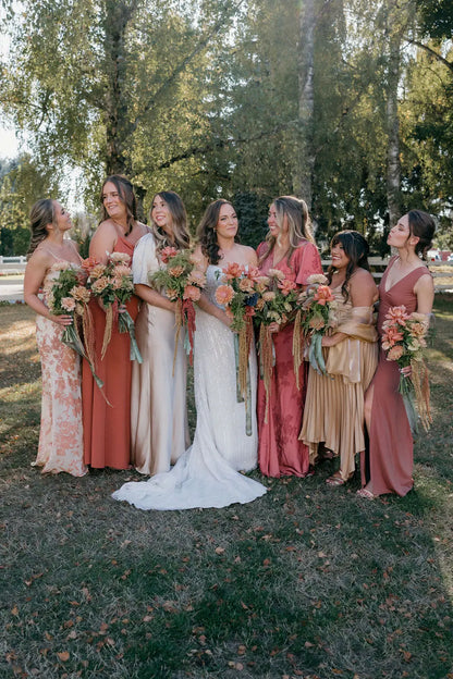Bride and bridesmaids in mismatched rust and champagne dresses with fall bouquets.
