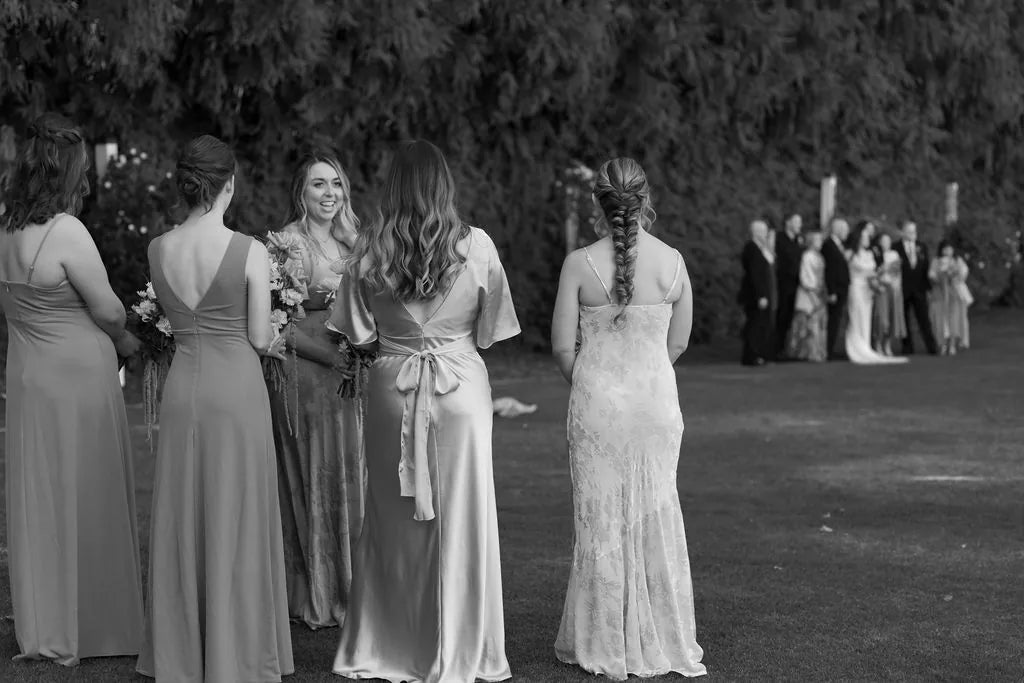 Black and white photo of bridesmaids from behind holding fall bouquets in mismatched dresses.