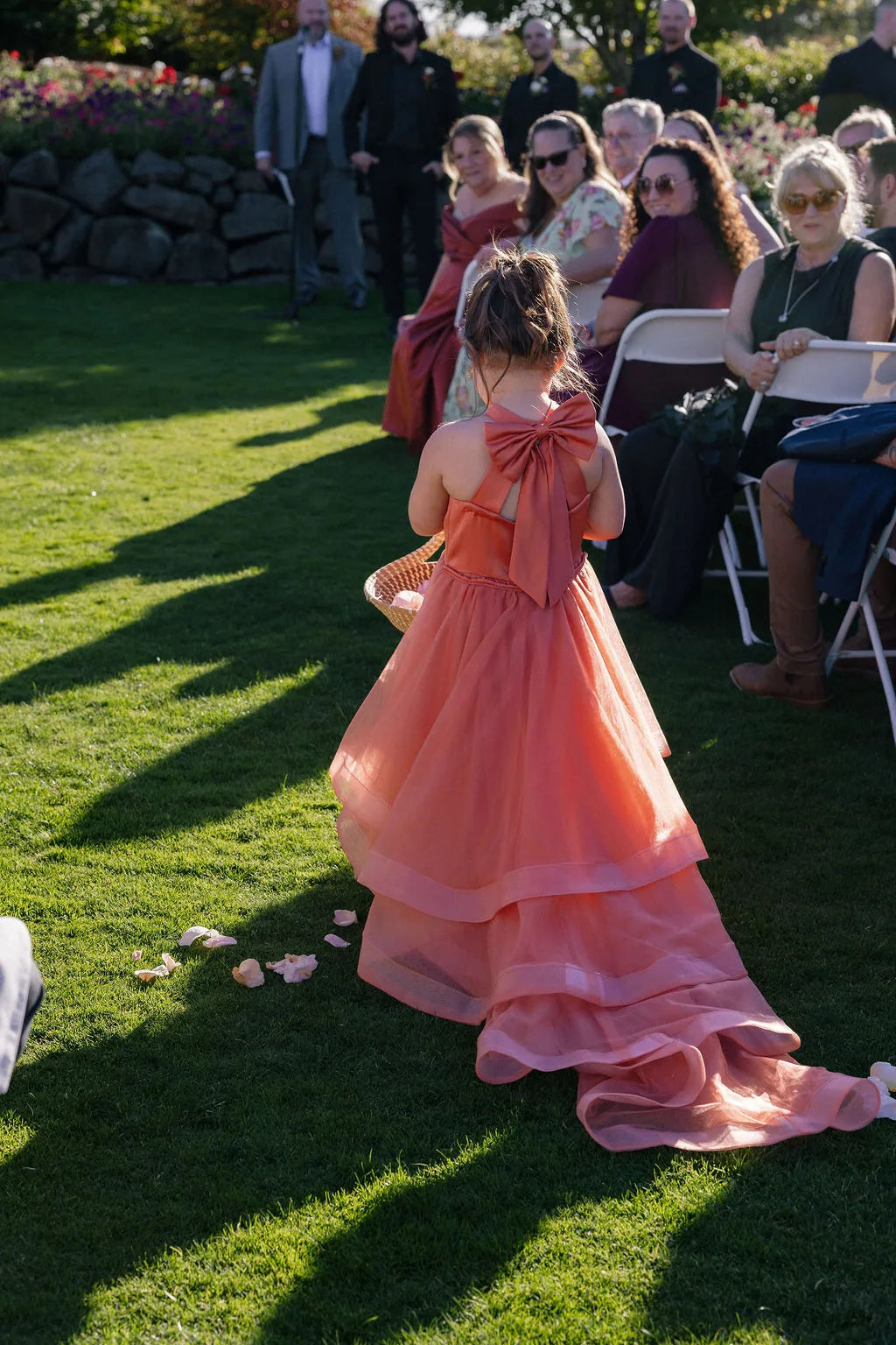 Flower girl in terracotta dress throwing rose petals at an outdoor fall ceremony.