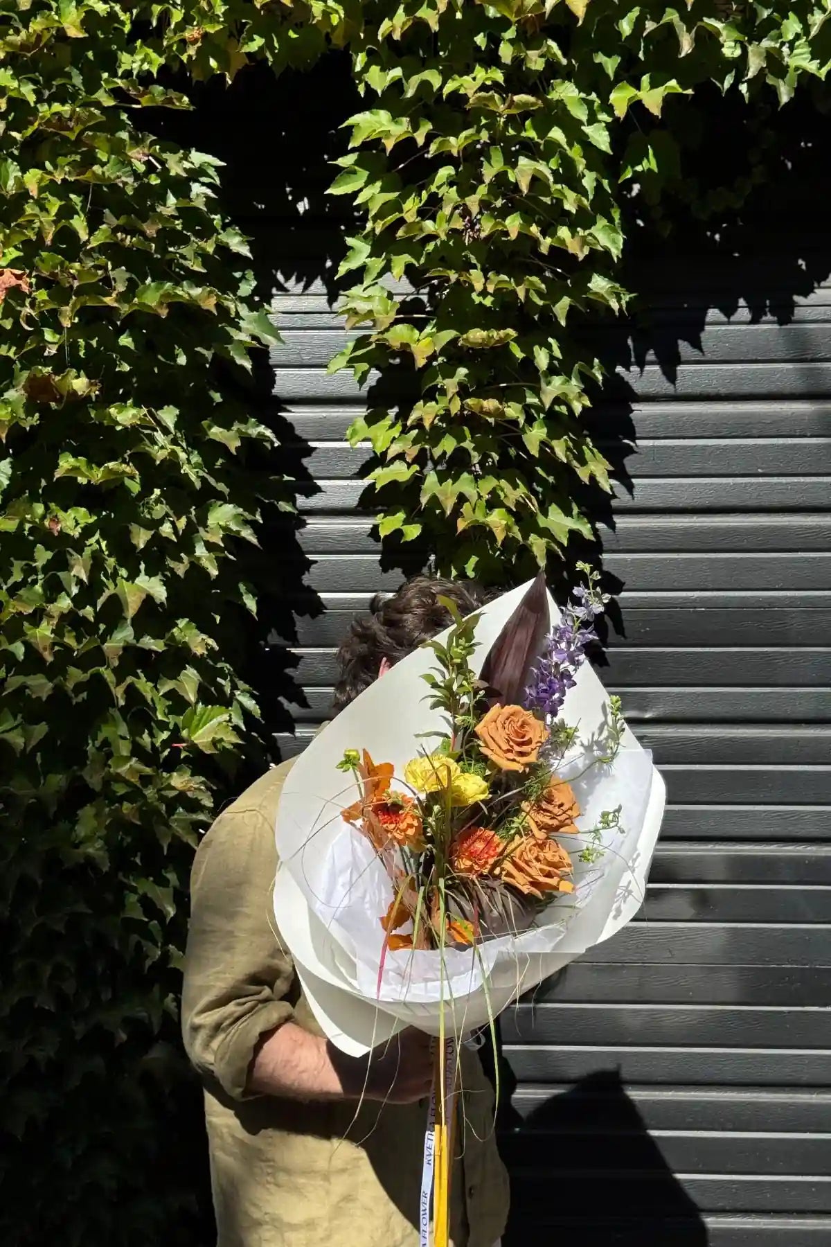 Fresh seasonal bouquet small size with autumn roses, purple delphinium and yellow accents wrapped in white paper by Kvetka Flower