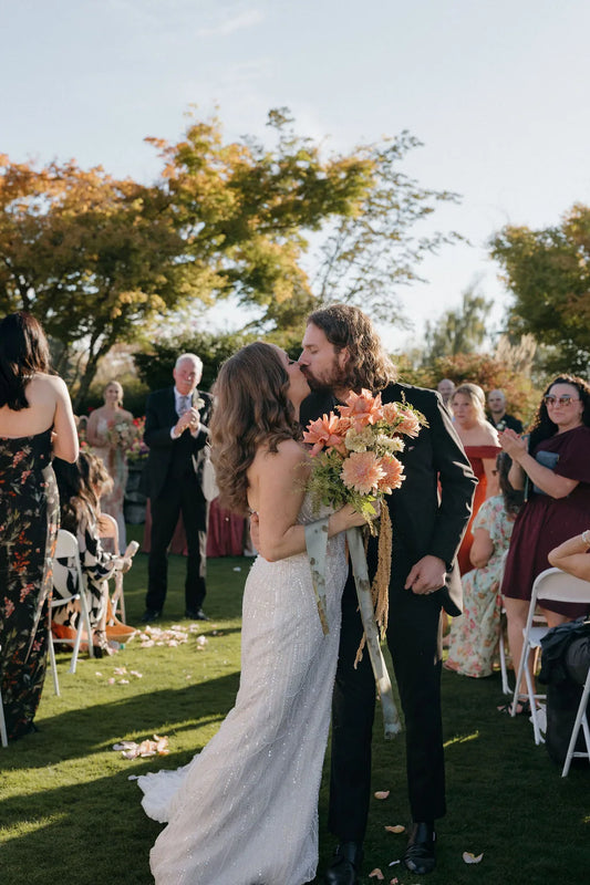Bride and groom kiss at Langdon Farms wedding ceremony holding trailing bridal bouquet.