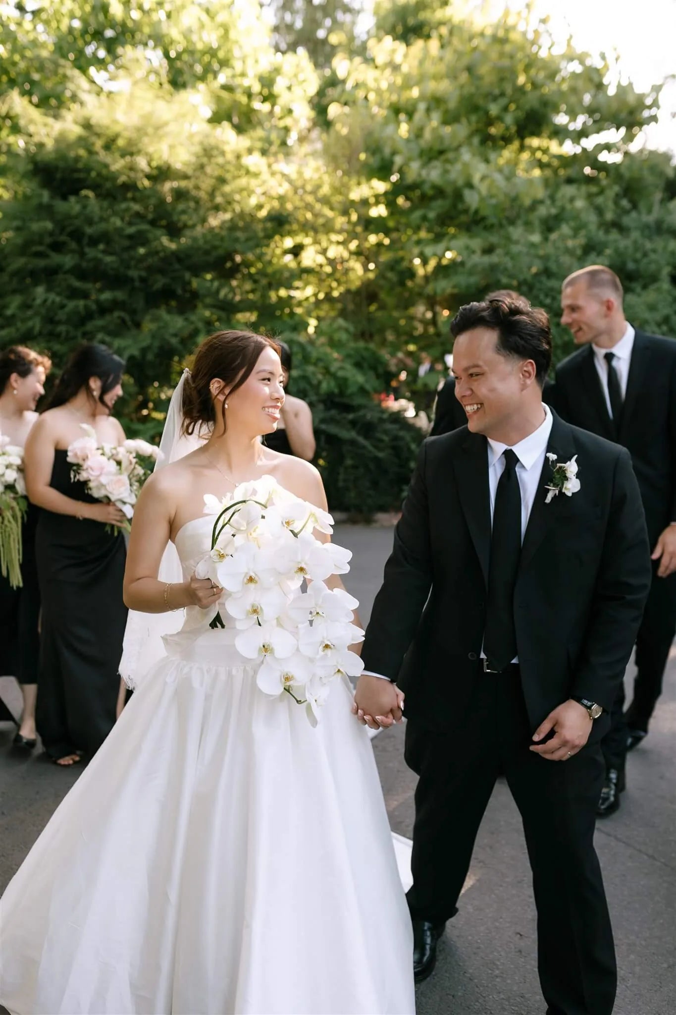 Happy bride and groom walking after ceremony with white orchid bouquet and boutonniere by Kvetka Flower