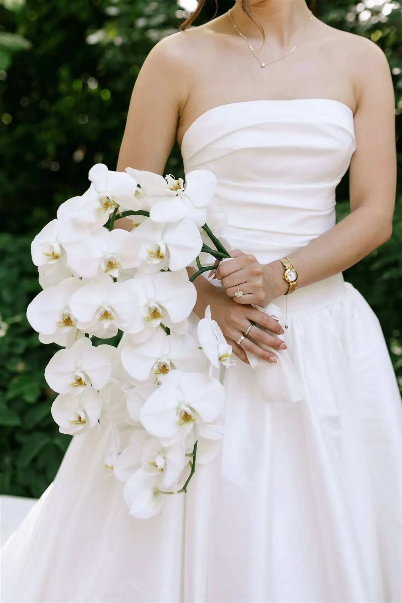 Cascading white phalaenopsis orchid bridal bouquet held by bride in garden by Kvetka Flower Portland OR