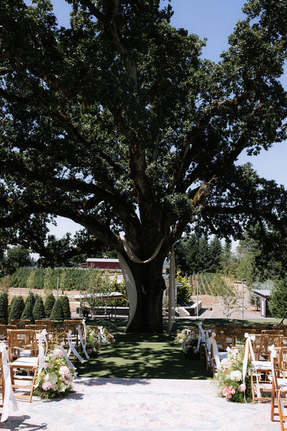 Outdoor wedding ceremony setup under a large tree with floral arrangements by Kvetka Flower at Redland Family Farm.