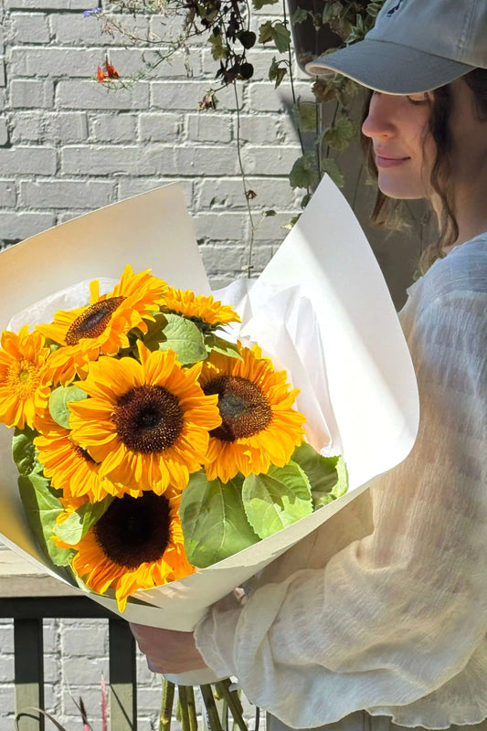Small sunflower bouquet held in hands, wrapped in soft white paper – Sun Day by Kvetka Flower, Portland Oregon