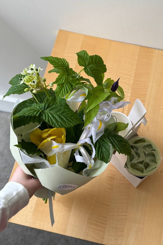 Small Mother's Day bouquet with white iris and yellow tulip from Kvetka Flower, paired with iced matcha from Tea Bar Portland, on wooden table.
