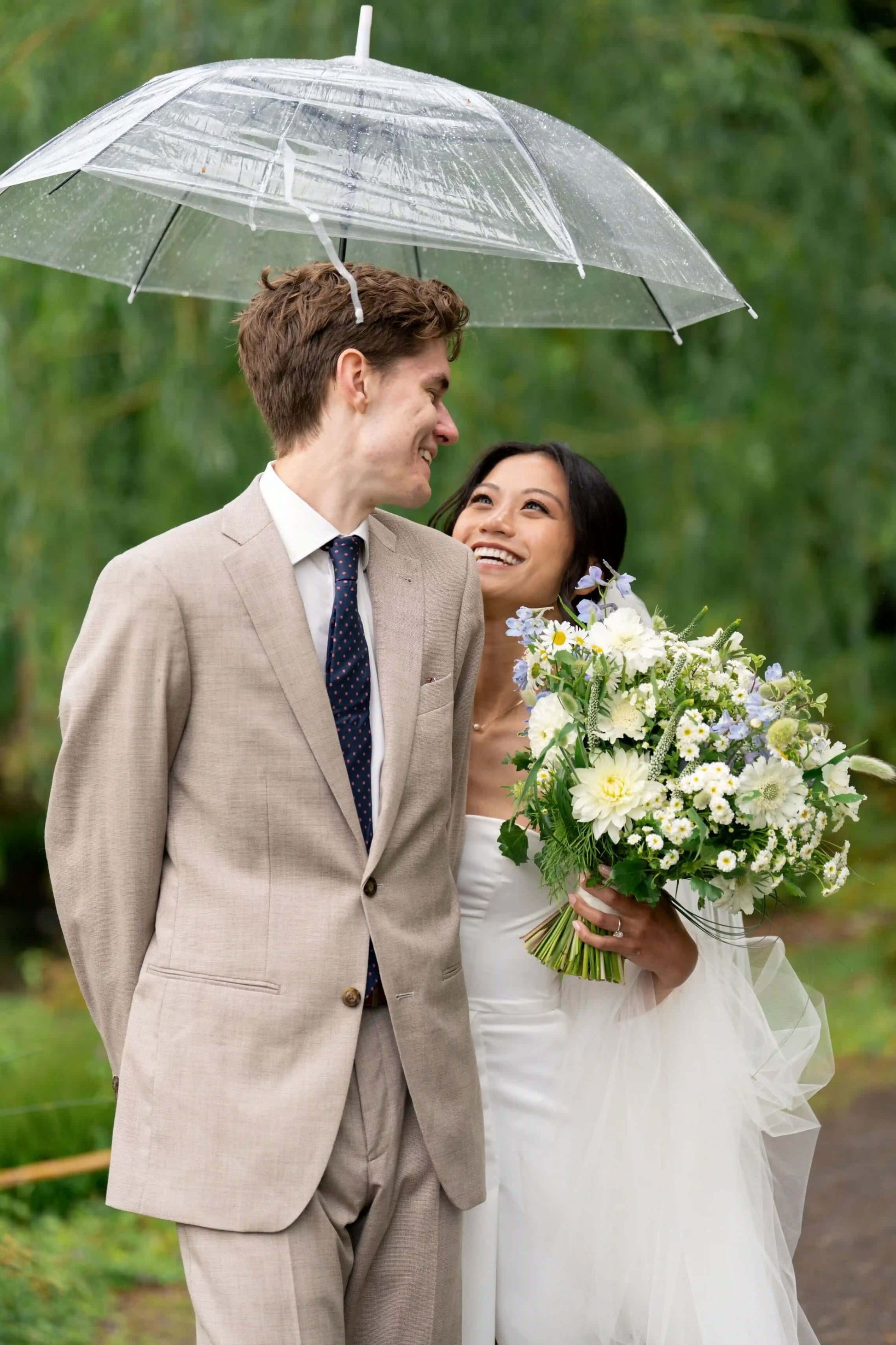 Bride and groom sharing an umbrella with a lush wedding bouquet by Kvetka Flower in Portland, OR