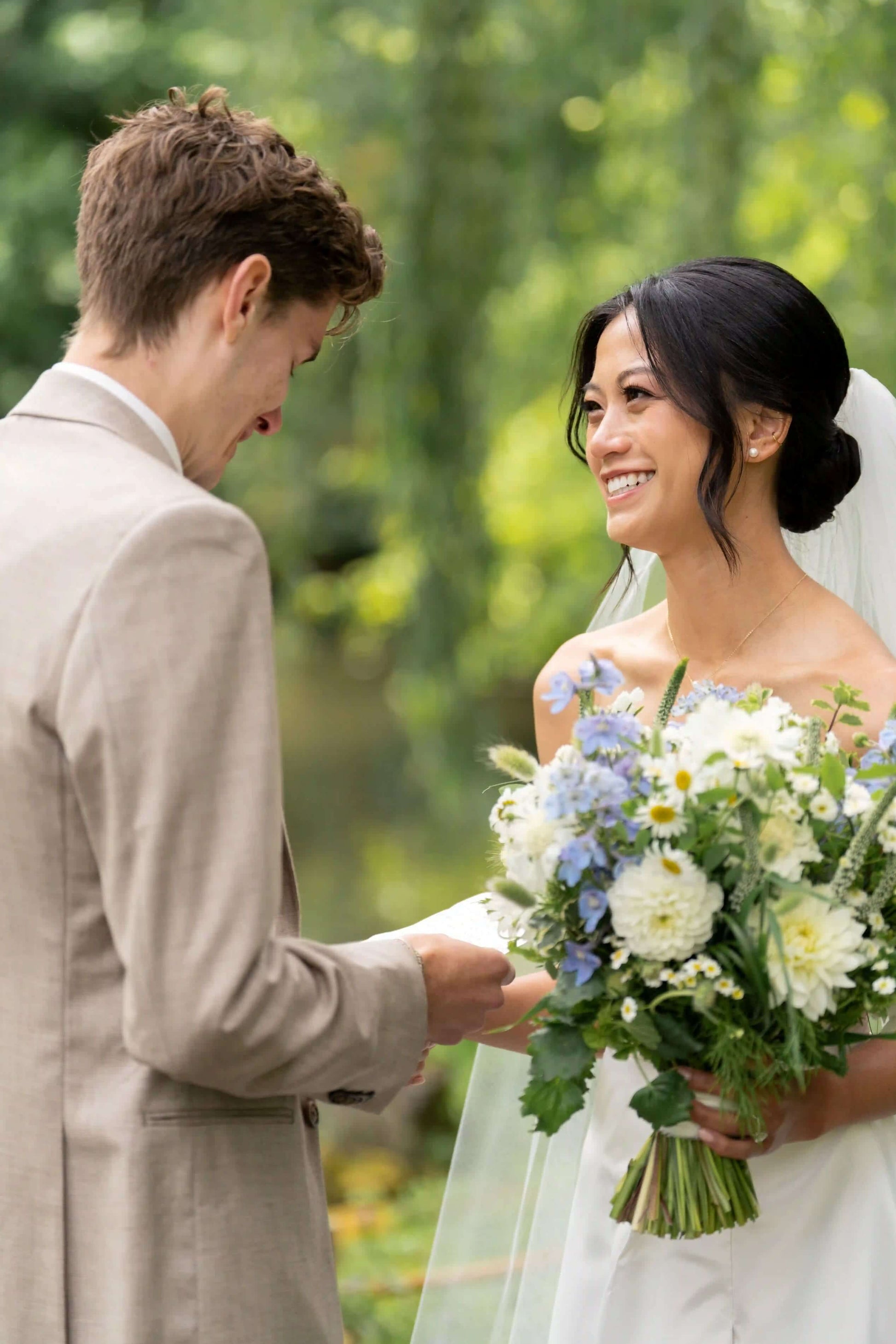 Bride smiling while holding a white and blue wedding bouquet by Kvetka Flower during vows in Portland, OR
