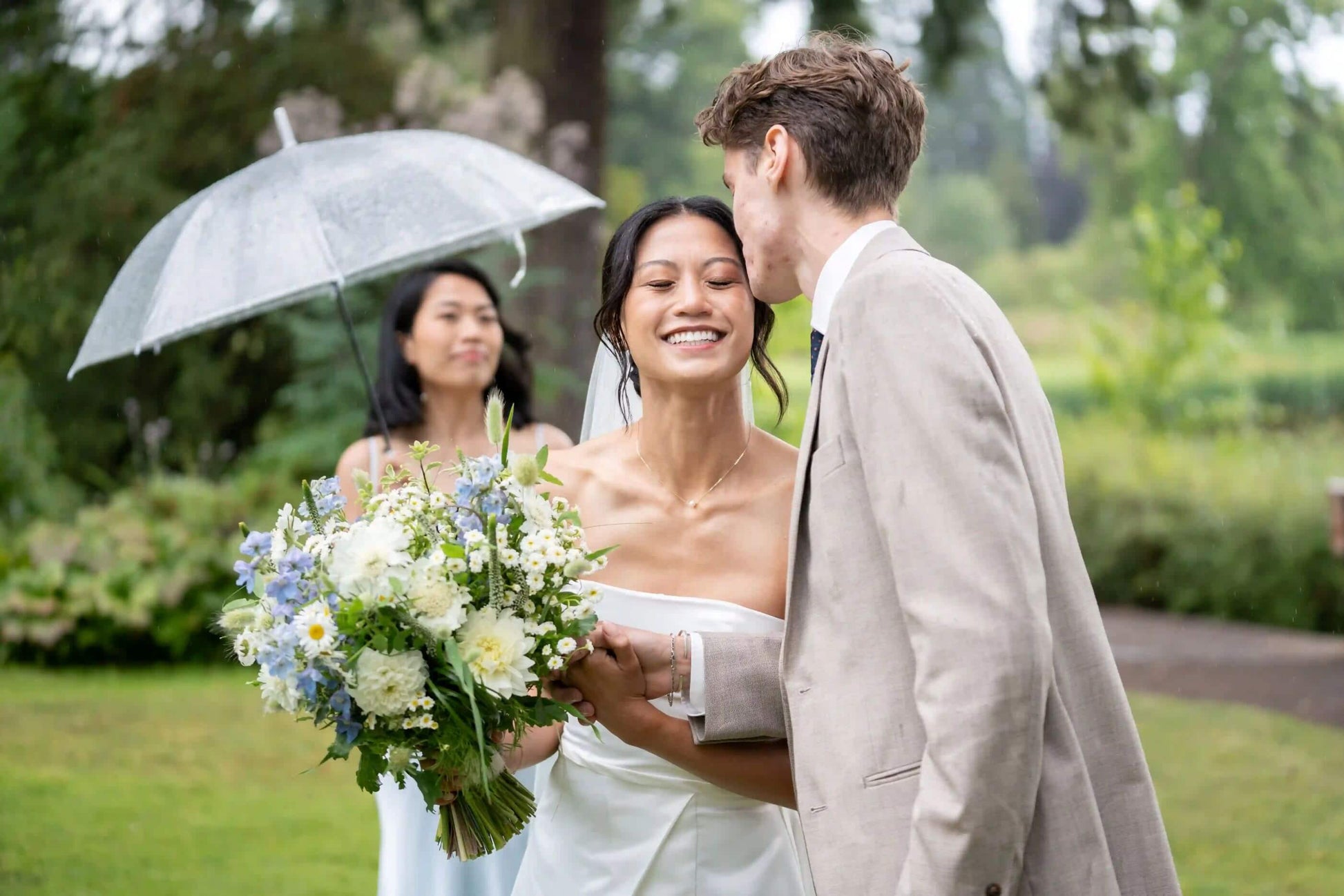 Bride and groom sharing a moment with Kvetka Flower bouquet while bridesmaid holds umbrella in Portland, OR