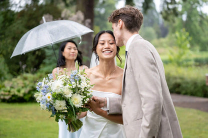Bride and groom sharing a moment with Kvetka Flower bouquet while bridesmaid holds umbrella in Portland, OR