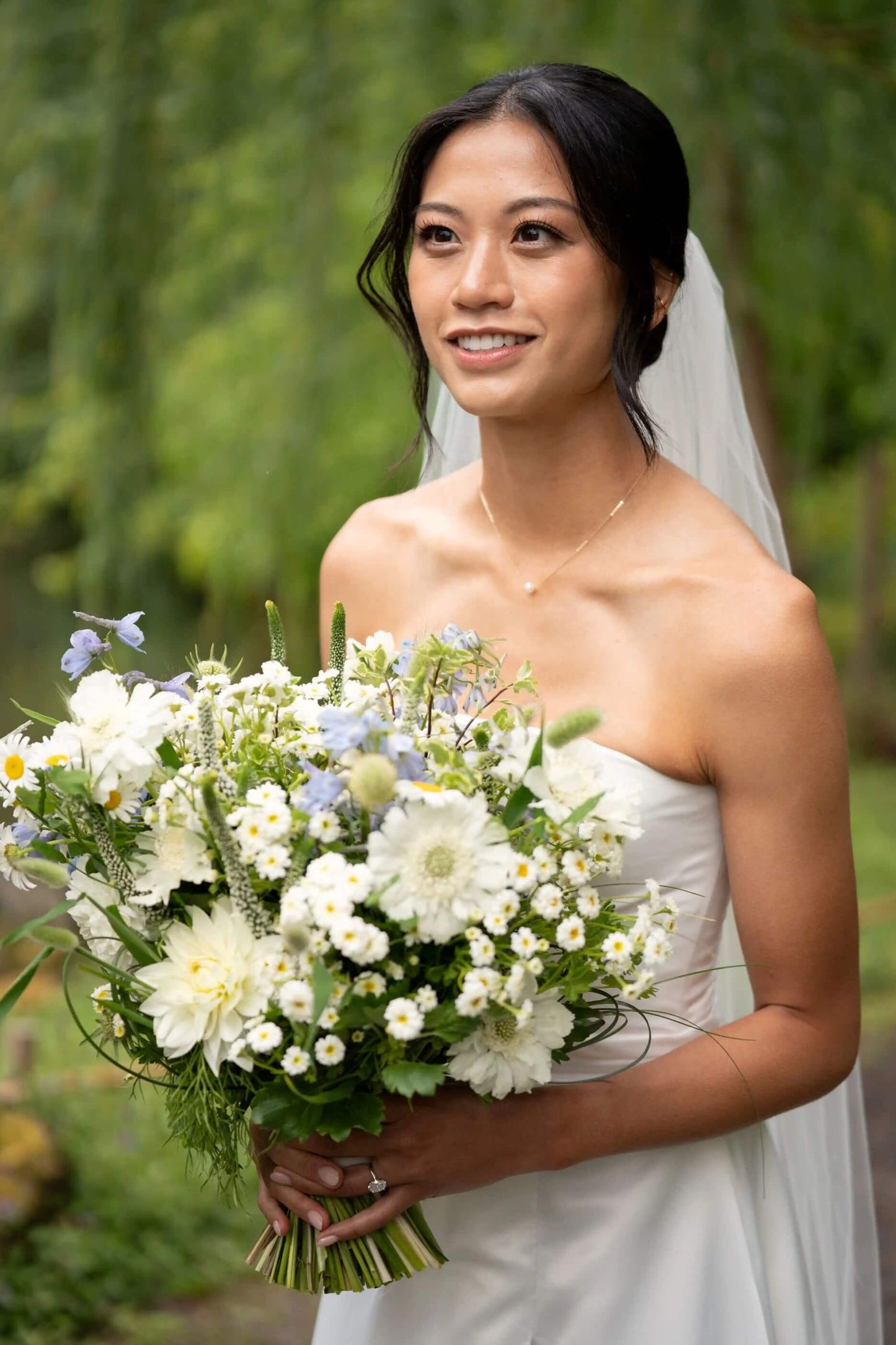 Bride smiling while holding a white and blue wedding bouquet by Kvetka Flower during vows in Portland, OR