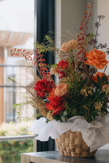 Seasonal flower basket with bright red and orange flowers displayed near window in natural light